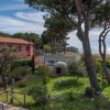 Vista di un edificio rosa, giardino e mare sullo sfondo.