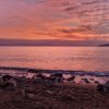 Tramonto rosa sul mare con spiaggia rocciosa.