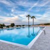 Piscina esterna con lettini e palme sotto un cielo blu.