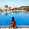 Una donna seduta sul bordo di una piscina circondata da lettini e ombrelloni.