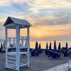 Torretta bianca sulla spiaggia al tramonto, ombrelloni blu chiusi.