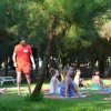 Gruppo fa yoga sul prato, istruttore in piedi, alberi sullo sfondo.