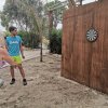 Due persone giocano a freccette all'aperto su un bersaglio di legno.