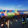 Spiaggia affollata con polveri colorate lanciate in aria durante un evento.