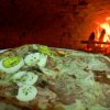 Pizza guarnita con uova e prosciutto cotto vicino a un forno a legna acceso.