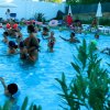 Persone in una piscina all'aperto, alcuni bambini sulle spalle degli adulti.