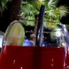 Bicchiere con bevanda rossa e fetta di lime, sfondo di palme notturne.
