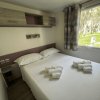 Letto matrimoniale con cuscini e asciugamani piegati, finestra con tende e armadietto sospeso.