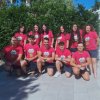 Un gruppo di persone posa sorridente indossando magliette rosa davanti a una siepe verde.