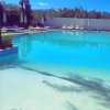 Grande piscina con acqua turchese e lettini intorno, ombrelloni chiusi e alberi sullo sfondo.