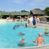Persone in piscina giocano a palla, ombrelloni sullo sfondo.