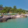 Spiaggia rocciosa con ombrelloni e mare limpido.