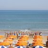 Spiaggia con ombrelloni e gruppo di persone in piedi a riva.